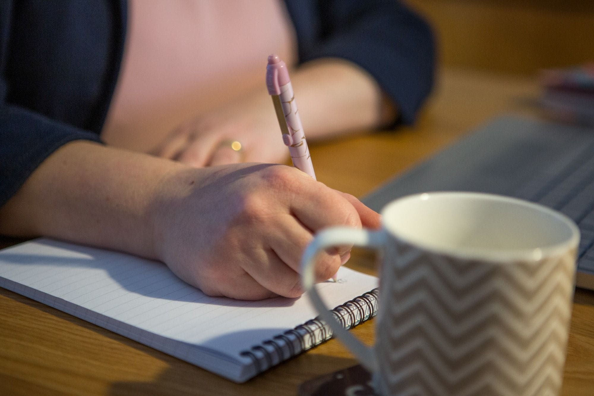 Lady writing on desk with notepad and cup